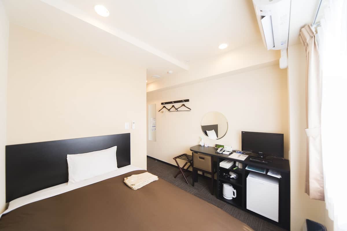 A hotel room with a bed, desk, chair, and a small kitchenette.