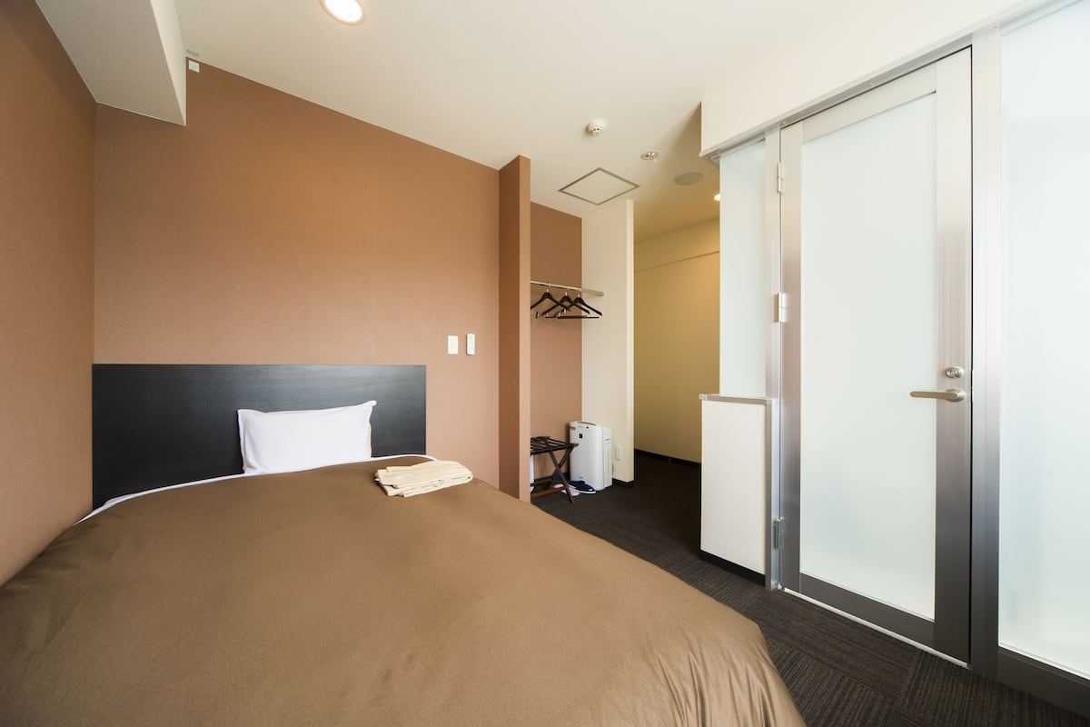 A hotel room with a large bed, a wardrobe, a desk, and a coat rack.