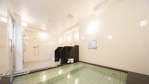 A modern indoor swimming pool with clear water, a black seating area, and white tiled walls. - Urbain Hiroshima Central (Hiroshima)