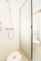 Un baño moderno con cabina de ducha de vidrio, inodoro y dispensador de jabón en la pared.