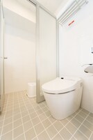 Un baño moderno con inodoro, cabina de ducha de vidrio y suelo de baldosas blancas.
