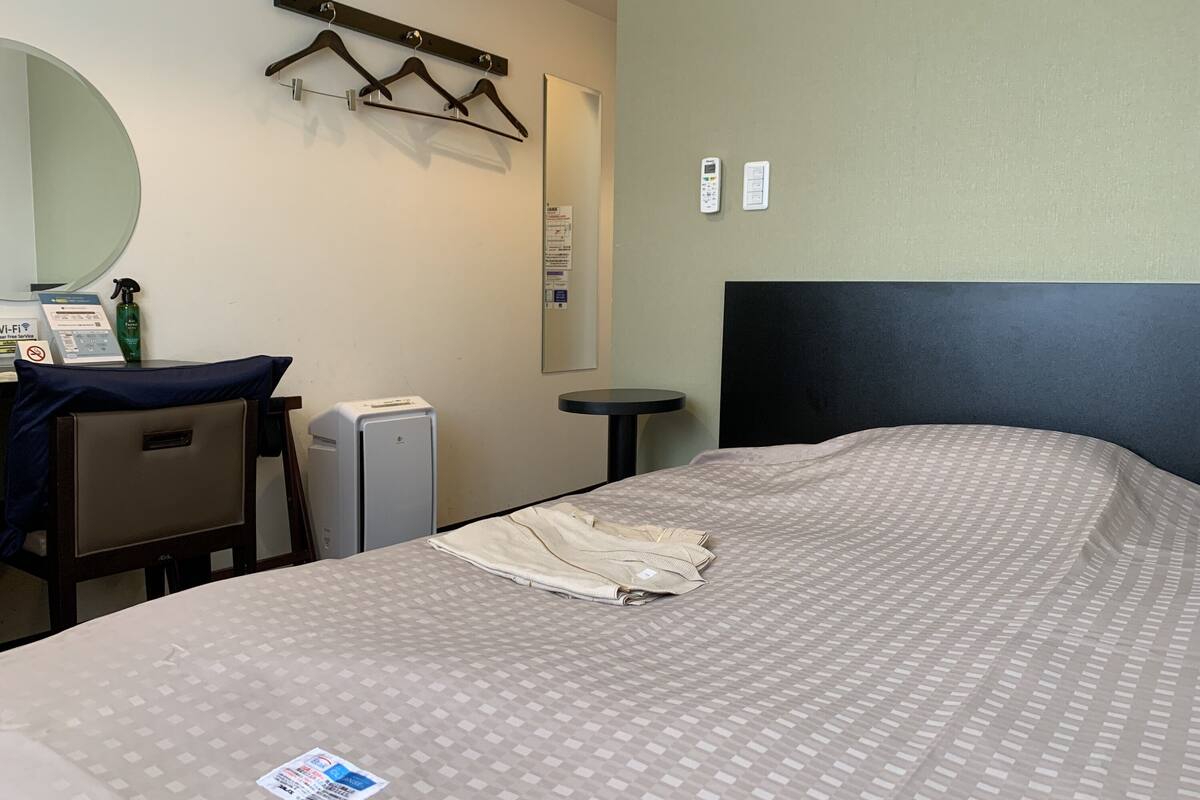 A hotel room with a bed, a desk, a chair, a mirror, and a small table.