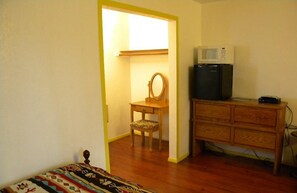 A small room with a bed, a wooden dresser, a chair, a mirror, and a microwave.