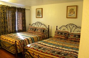 Una habitación con dos camas, cada una con una colcha estampada y almohadas a juego. Hay cortinas en la ventana y dos cuadros enmarcados en la pared.