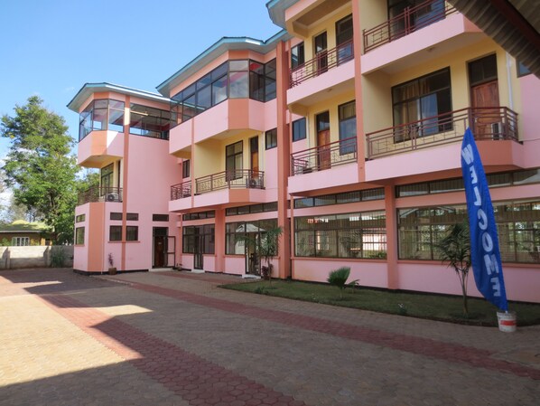 A multi-story building with balconies and large windows, featuring a welcoming sign. - Stella Maris Lodge (Moshi)