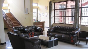 A spacious living room with leather sofas, a coffee table, and a staircase leading to an upper floor. - Stella Maris Lodge (Moshi)
