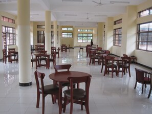 A spacious dining area with multiple tables and chairs, large windows with bars, and ceiling fans. - Stella Maris Lodge (Moshi)