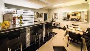 A modern kitchen with a black countertop, bar stools, and a dining area with a table and chairs. - Hotel KK (Itu)