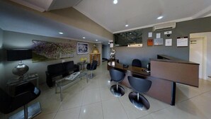 A modern hotel lobby with a reception desk, seating area, and a large floral artwork on the wall. - Hotel KK (Itu)