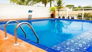 A swimming pool with a blue tiled edge, metal handrails, and a white wall in the background. - Hotel KK (Itu)