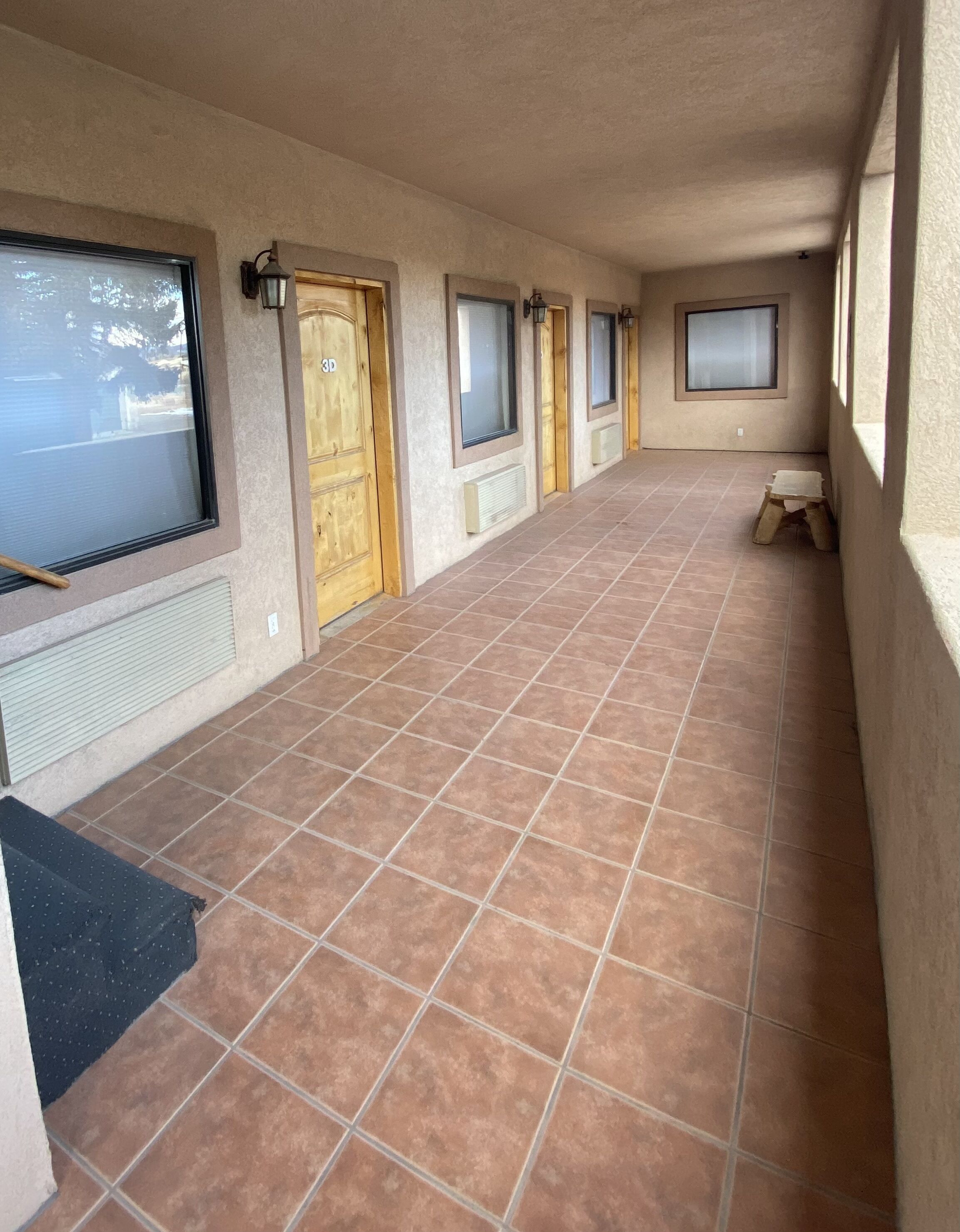 Un pasillo con piso de baldosas, puertas de madera y ventanas.
