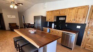 A modern kitchen with wooden cabinets, a stainless steel refrigerator, and a central island with stools. - The Snuggle Inn (Loa)