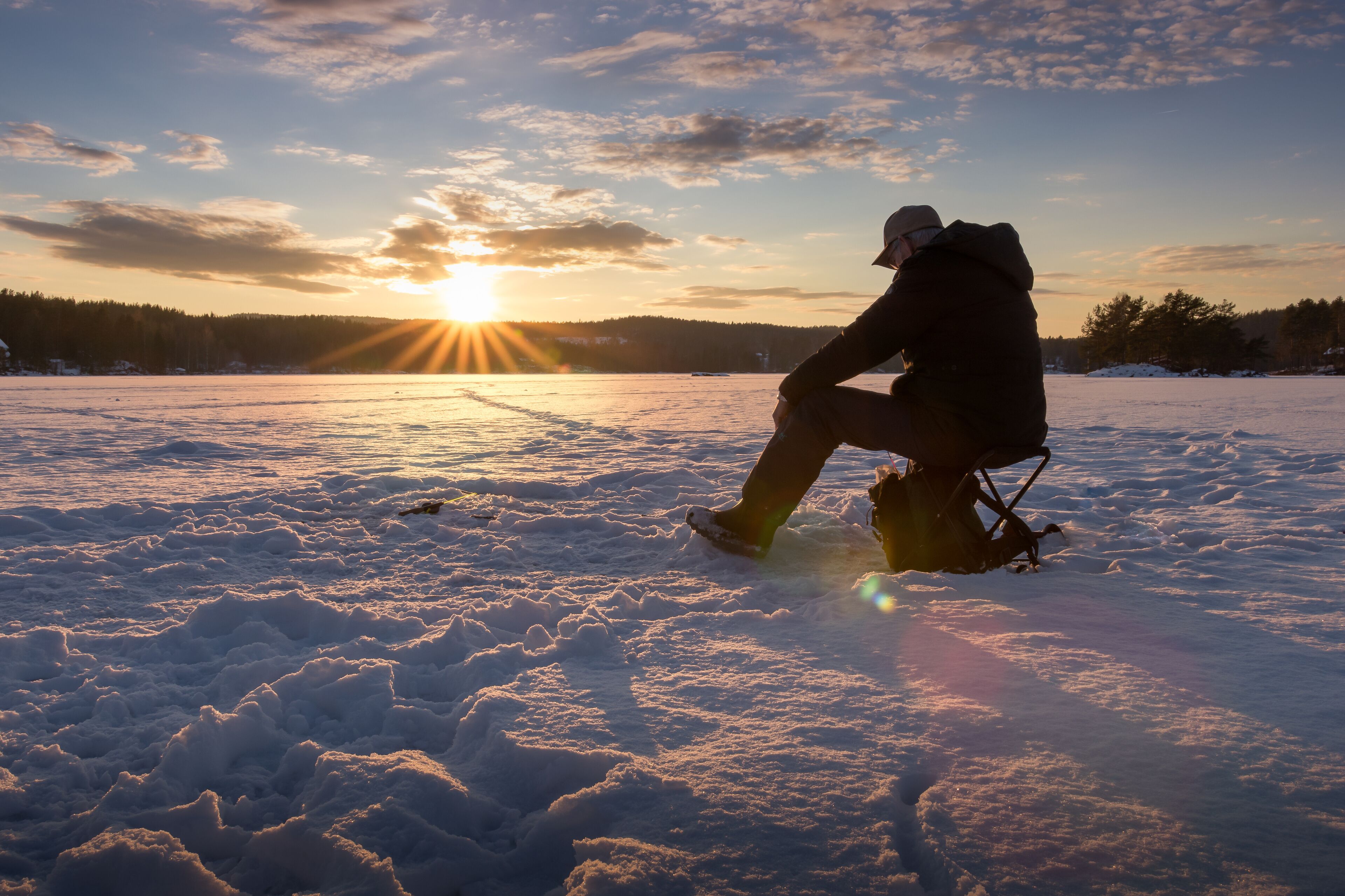 A person sitting on a sled in a snowy field with the sun setting in the background.