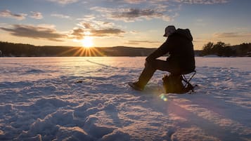 Una persona sentada en un trineo en un campo nevado con el sol poniéndose al fondo.