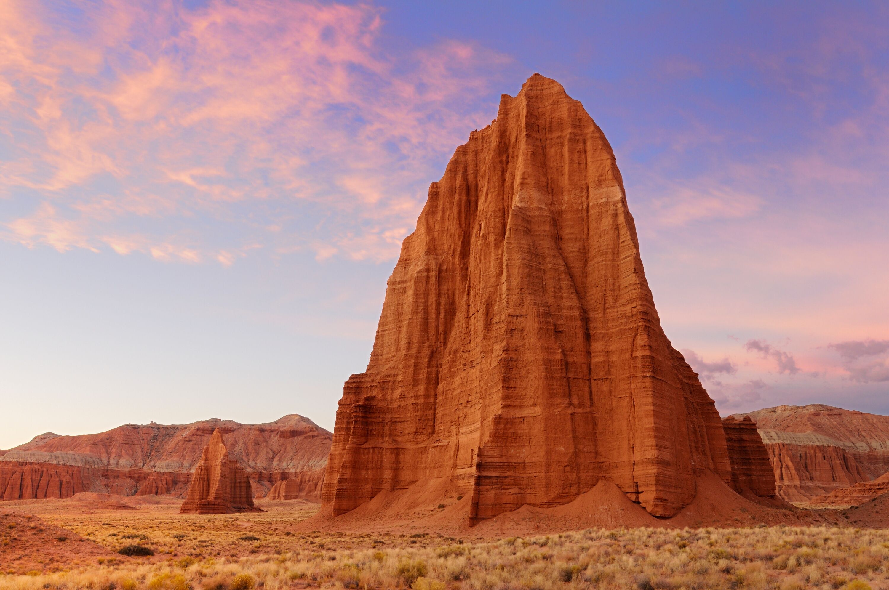 A large, red rock formation in a desert landscape.