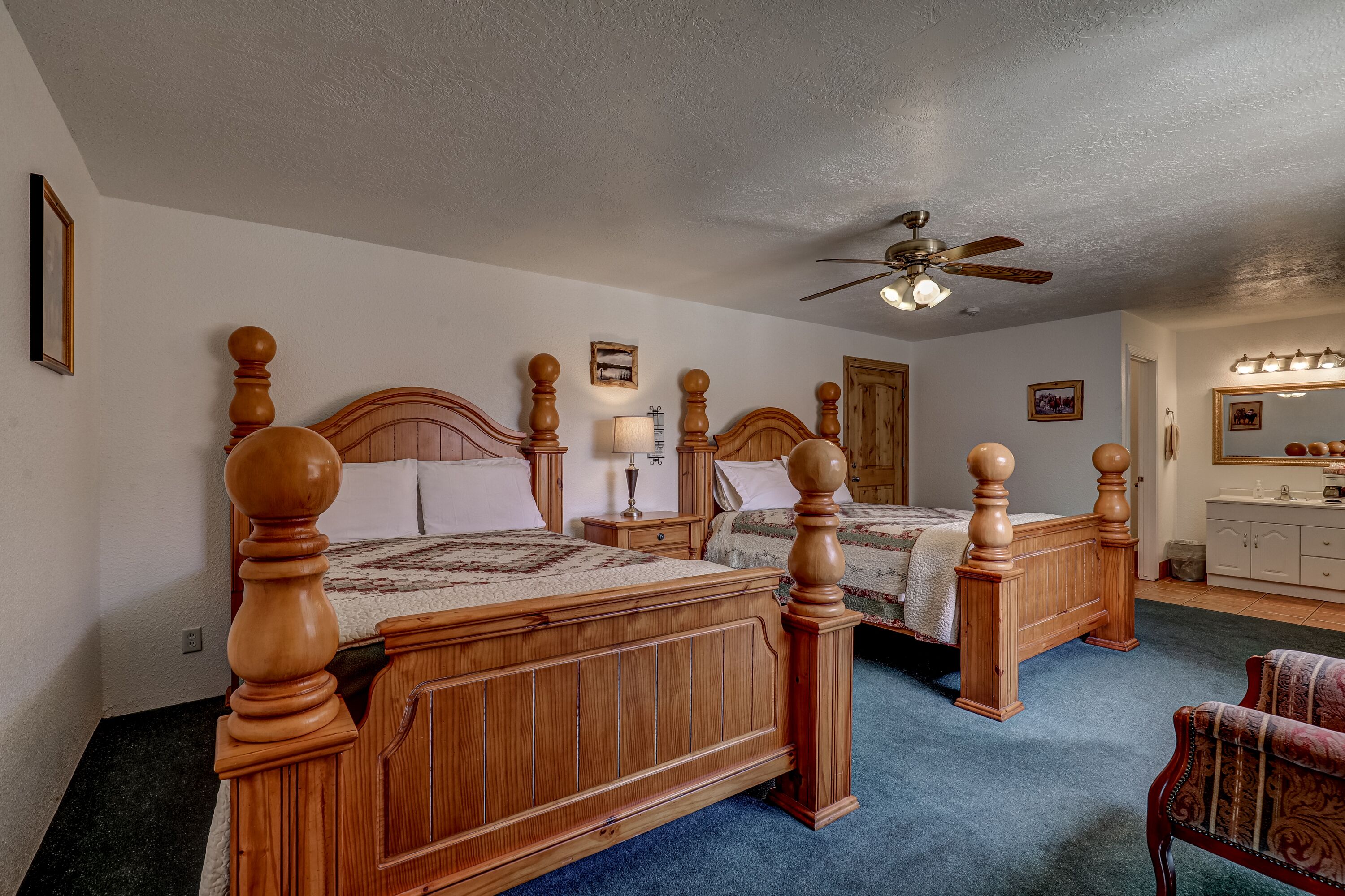 Een slaapkamer met twee houten bedden, een plafondventilator, een dressoir en een stoel.