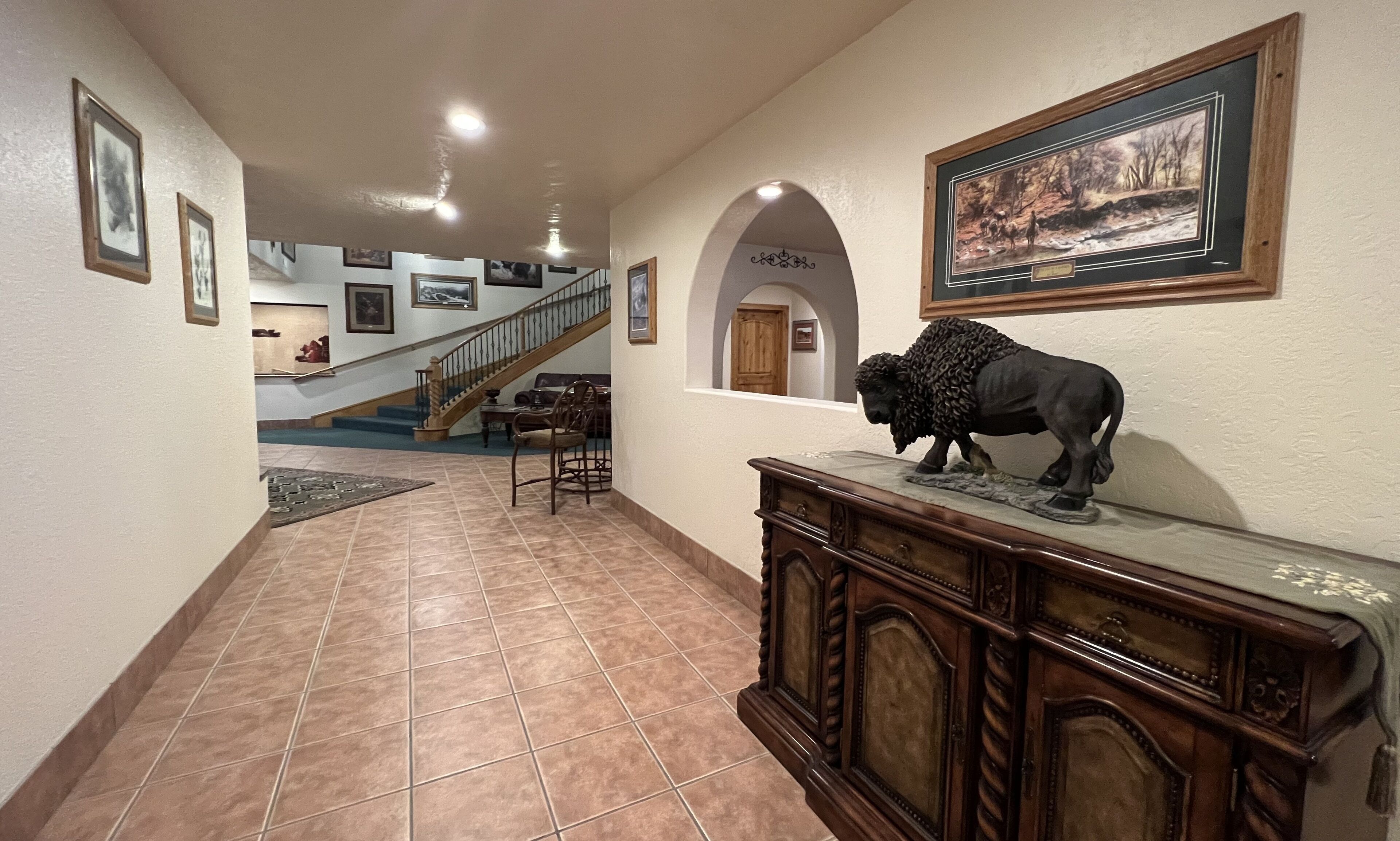 Um corredor com escada, um armário de madeira com uma escultura de búfalo e quadros nas paredes.