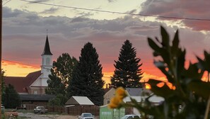 A church with a steeple, surrounded by tall trees and a sunset in the background.