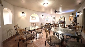 A dining area with round tables and chairs, arched windows, and wall-mounted lighting. - The Snuggle Inn (Loa)