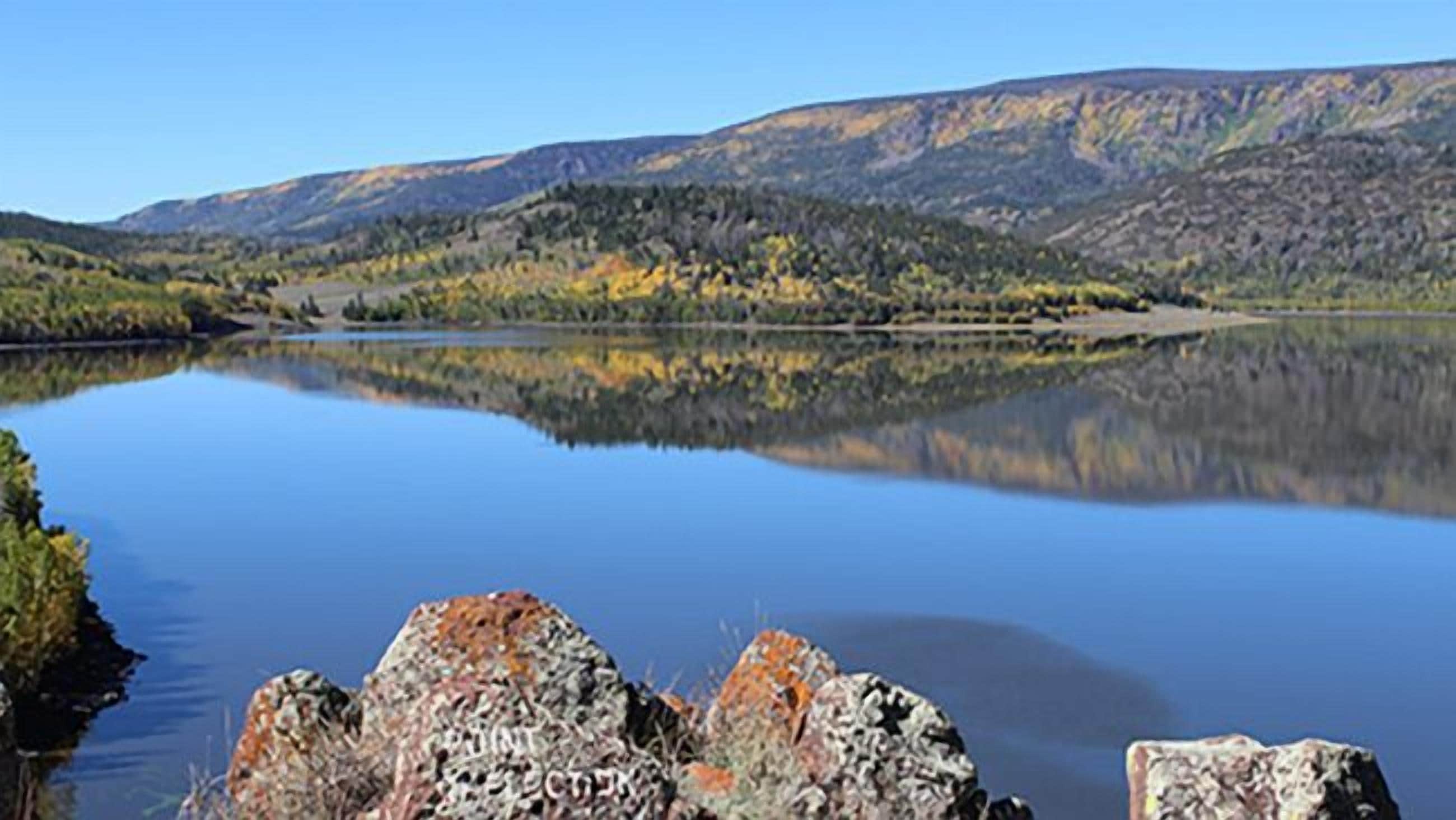 A calm lake with a rocky shoreline and a mountainous backdrop.