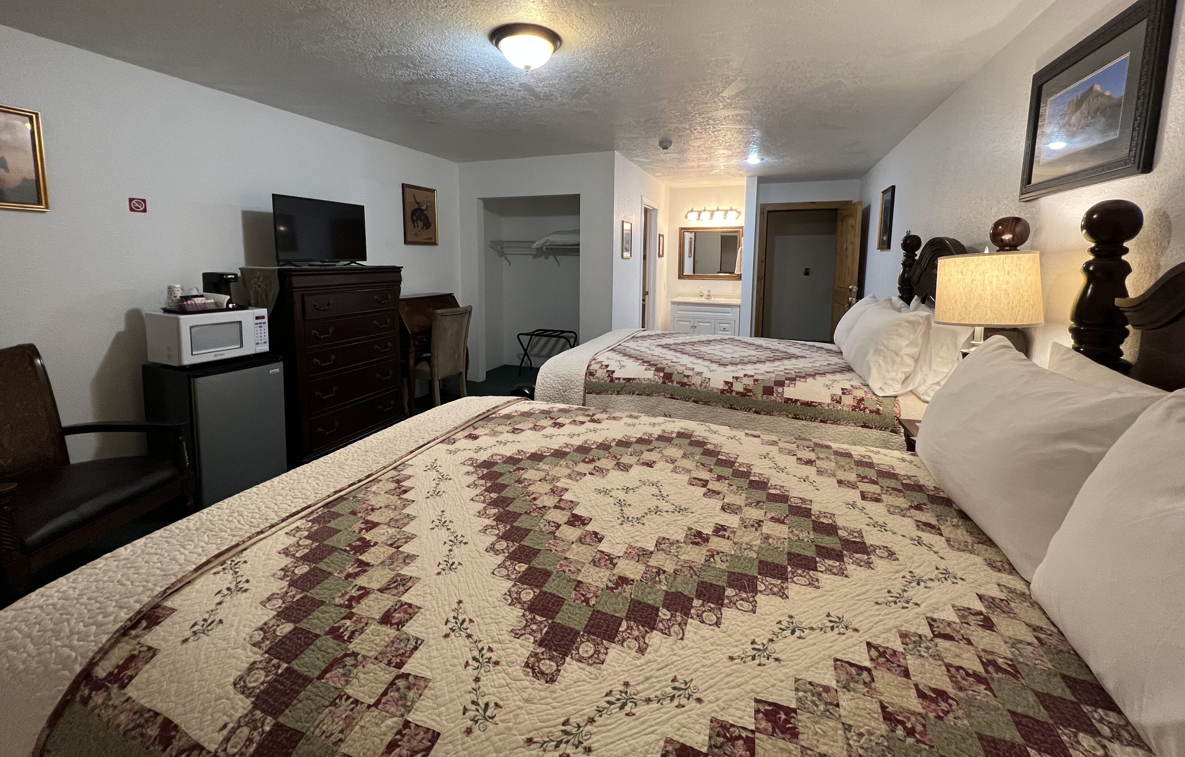 Een hotelkamer met twee bedden, een dressoir, een magnetron, een televisie en een spiegel.