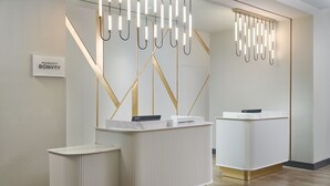 A reception area with two white reception desks, a sign reading "Marriott Bonvoy," and a modern chandelier.