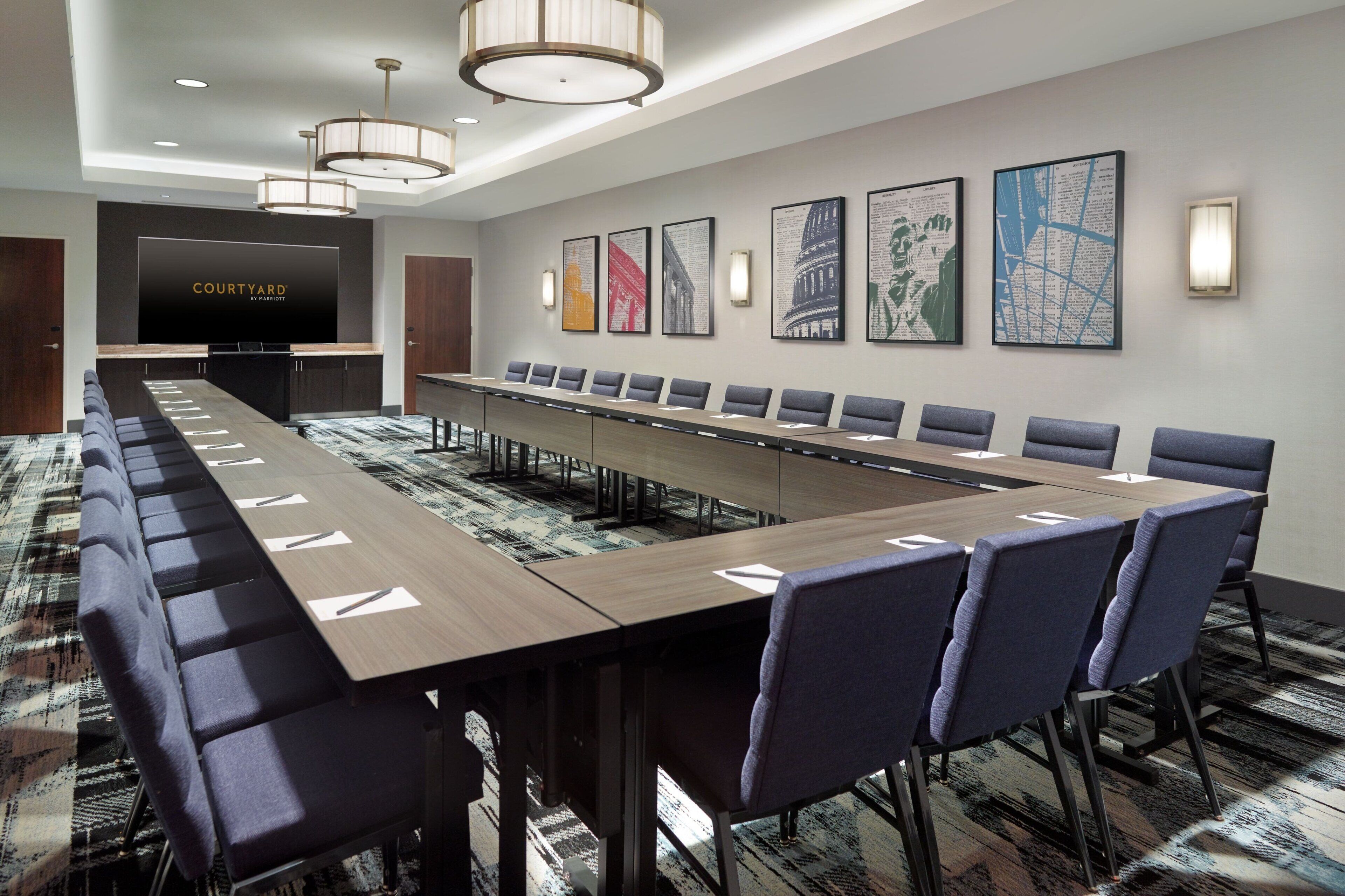 A conference room with a long table, multiple chairs, a TV screen, and framed artwork on the wall.