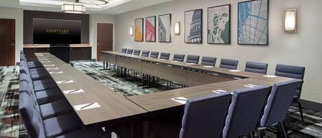 A conference room with a long table, multiple chairs, a TV screen, and framed artwork on the wall.