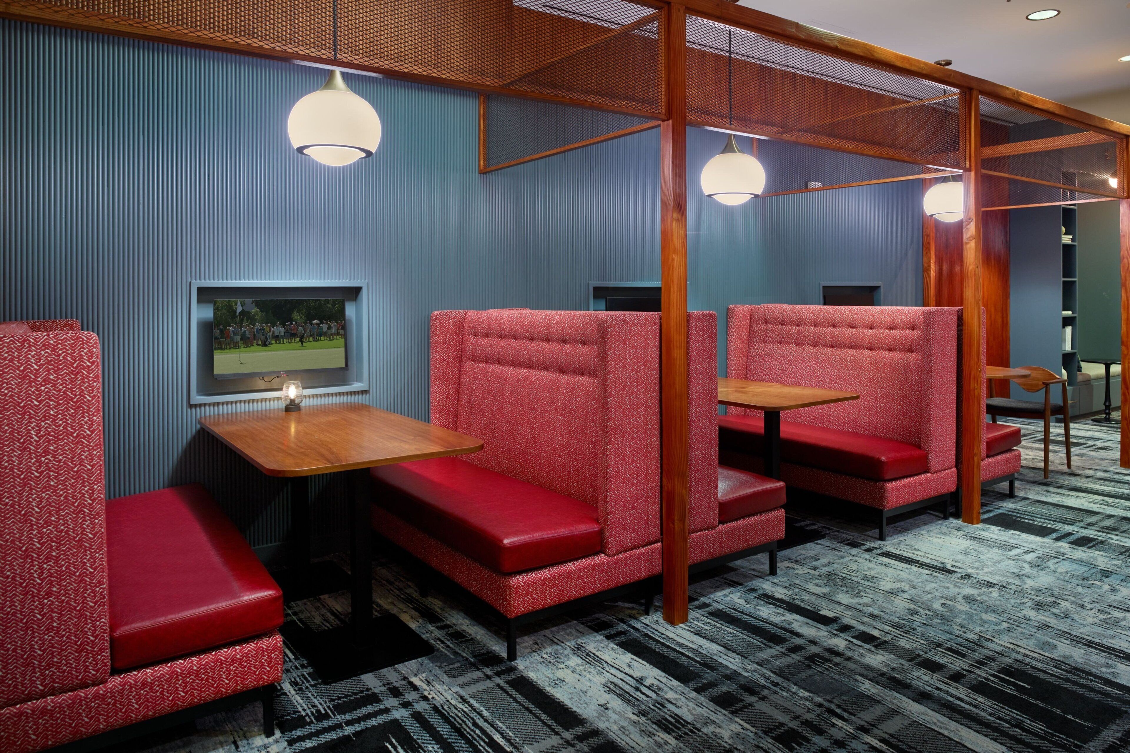 A room with red upholstered seating, a wooden table, and a television mounted on the wall.