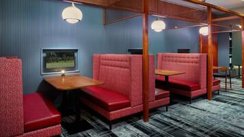 A room with red upholstered seating, a wooden table, and a television mounted on the wall.