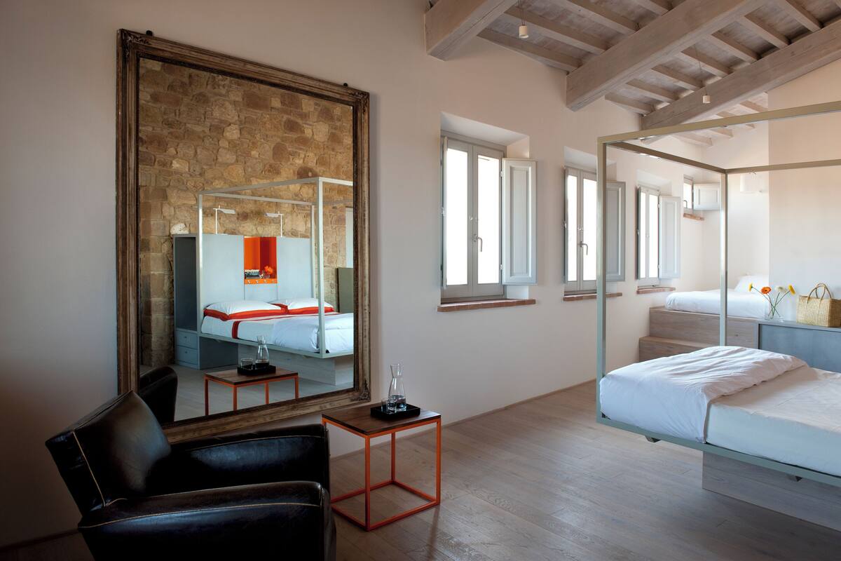 A modern hotel room with a large mirror, a bed, a small table, and a chair.