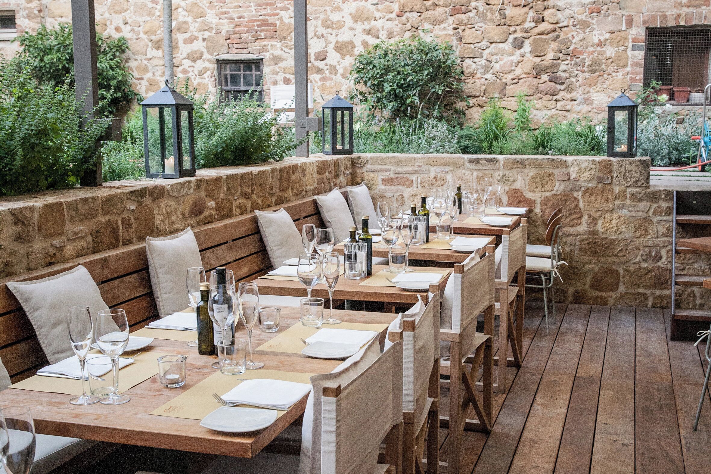 An outdoor dining area with wooden tables and benches, stone walls, and potted plants.