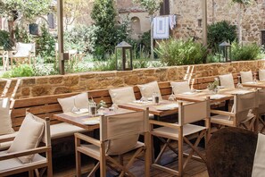 An outdoor dining area with wooden tables and benches, stone walls, and greenery. - La Bandita Townhouse (Pienza)