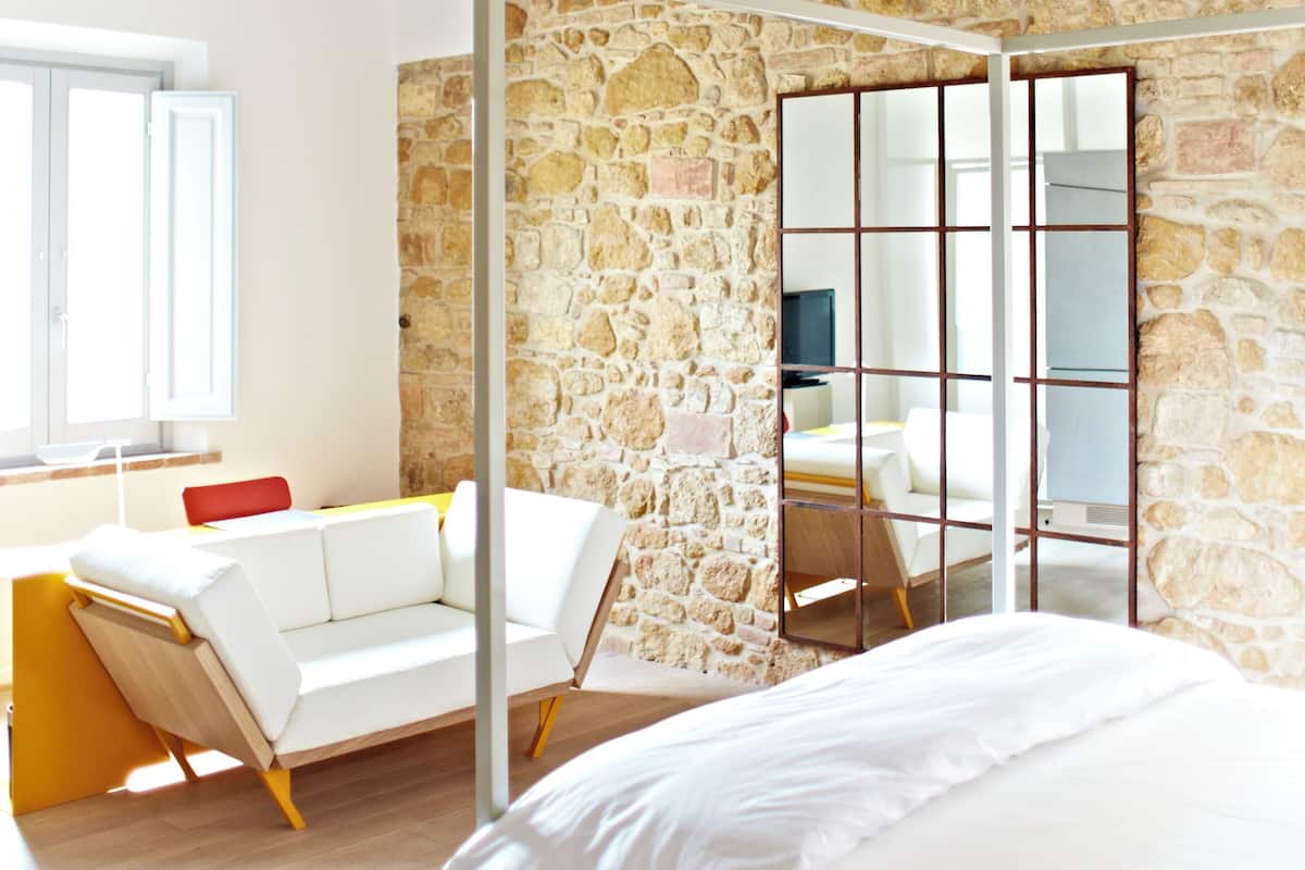 A bedroom with a bed, a stone wall, a wooden ceiling, and a window.