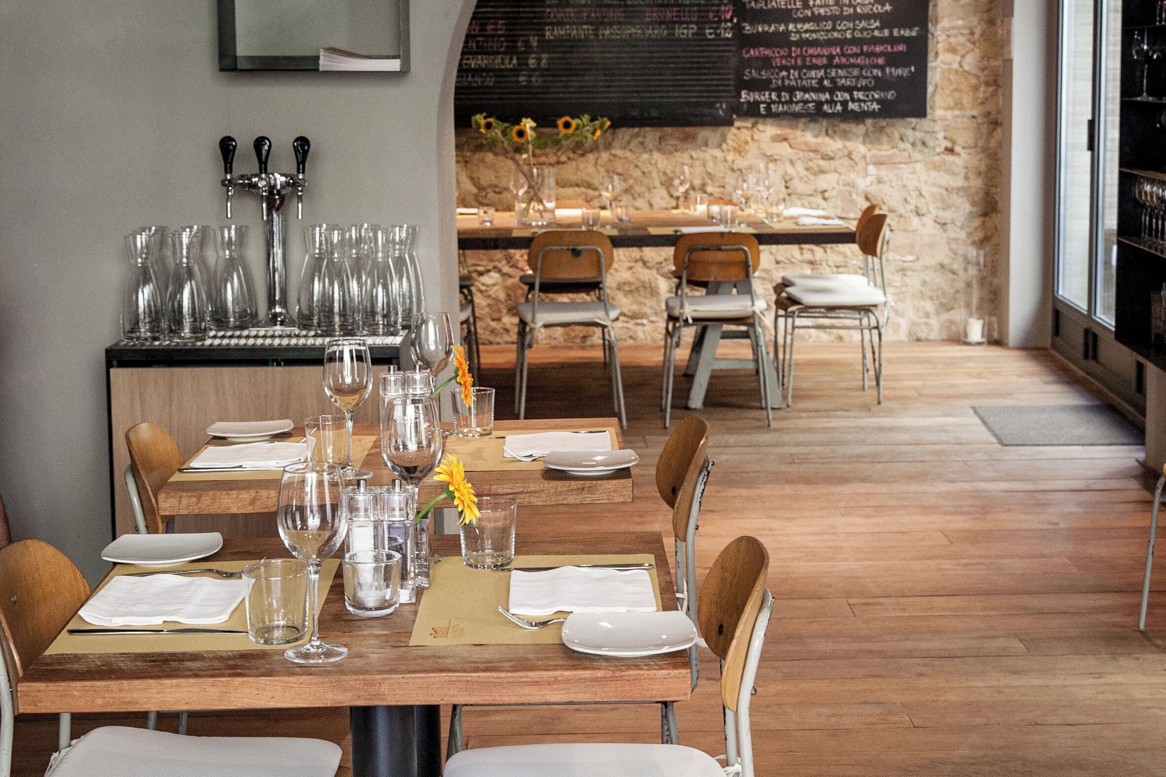 A restaurant interior with wooden tables, chairs, and a bar area with taps and glasses.