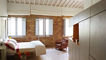 A bedroom with a stone wall, a bed with white linens, a wooden floor, and a window with white shutters.