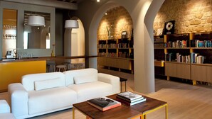 Um interior moderno com sofá branco, mesa de centro de madeira e estantes cheias de livros.