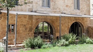 Um pátio com um edifício de pedra, aberturas em arco e uma área de estar coberta.
