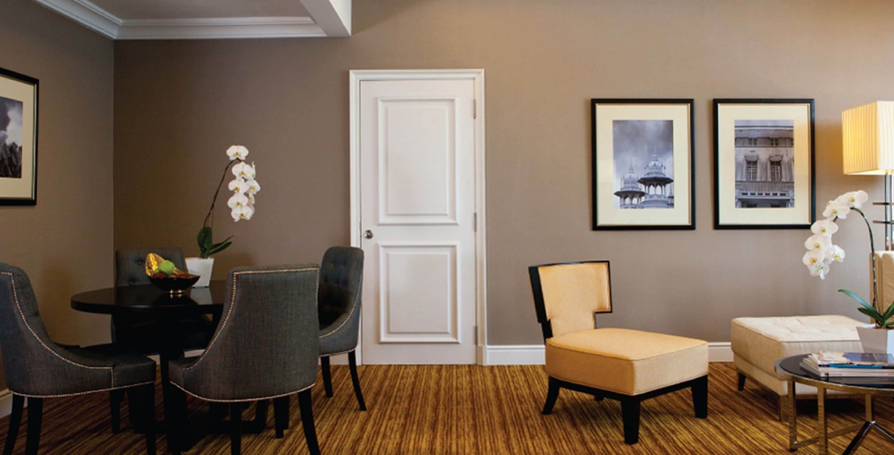 A hotel room with a dining area, a sofa, a chair, and two framed pictures on the wall.