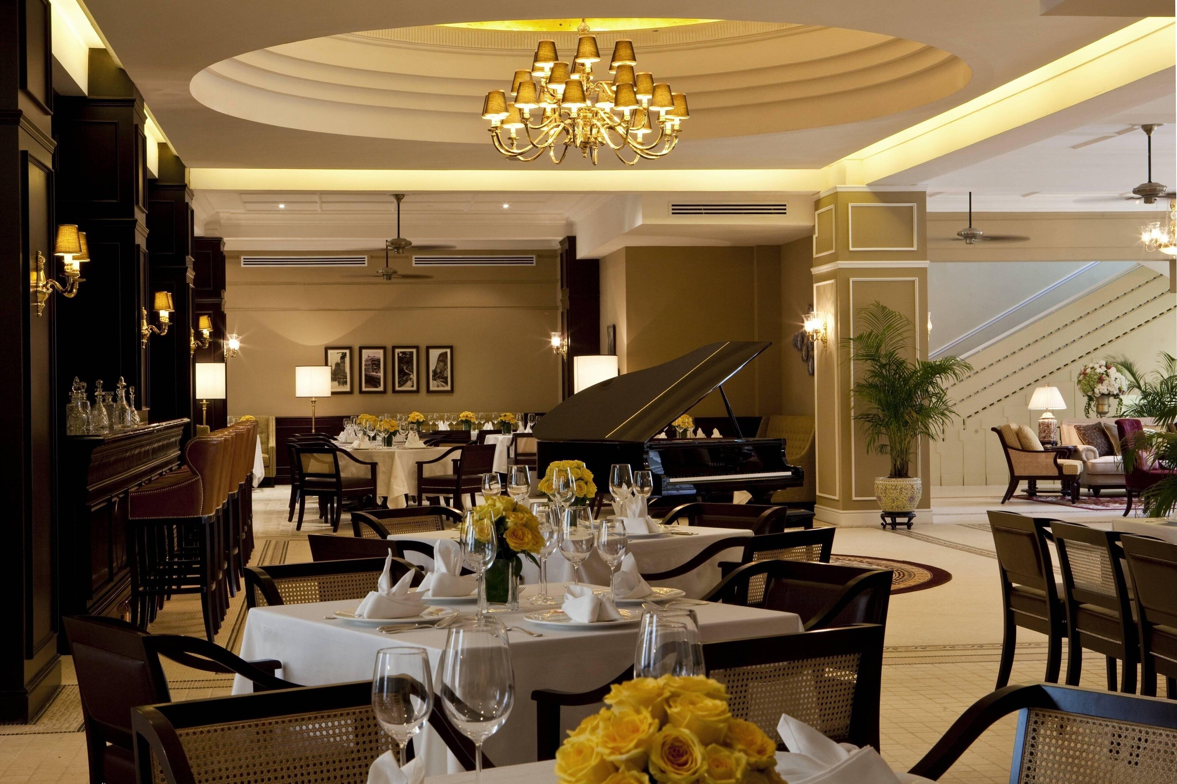 A formal dining area with tables set for service, a grand piano, and a chandelier.