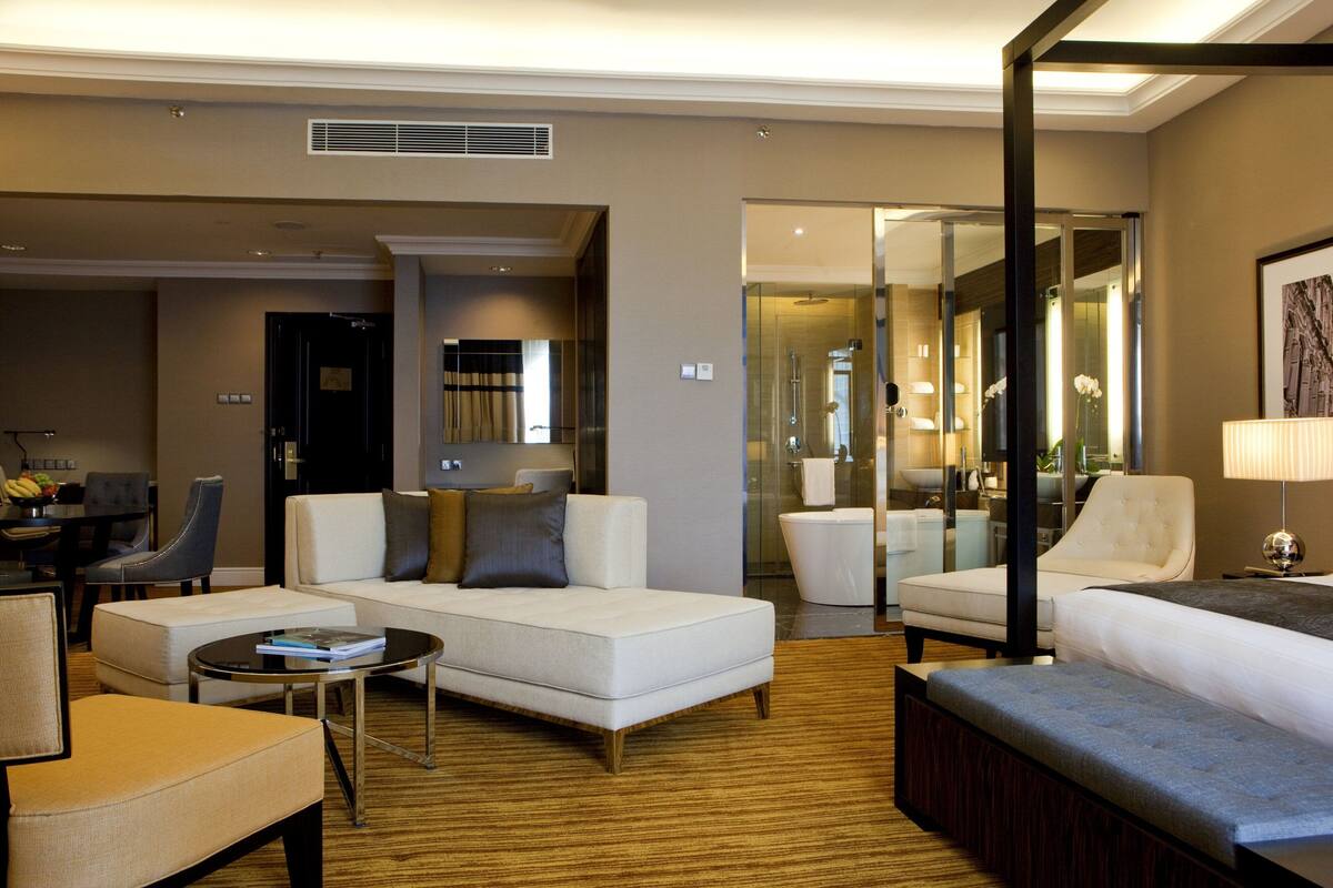 A modern hotel room with a sofa, armchairs, a coffee table, and a large mirror.