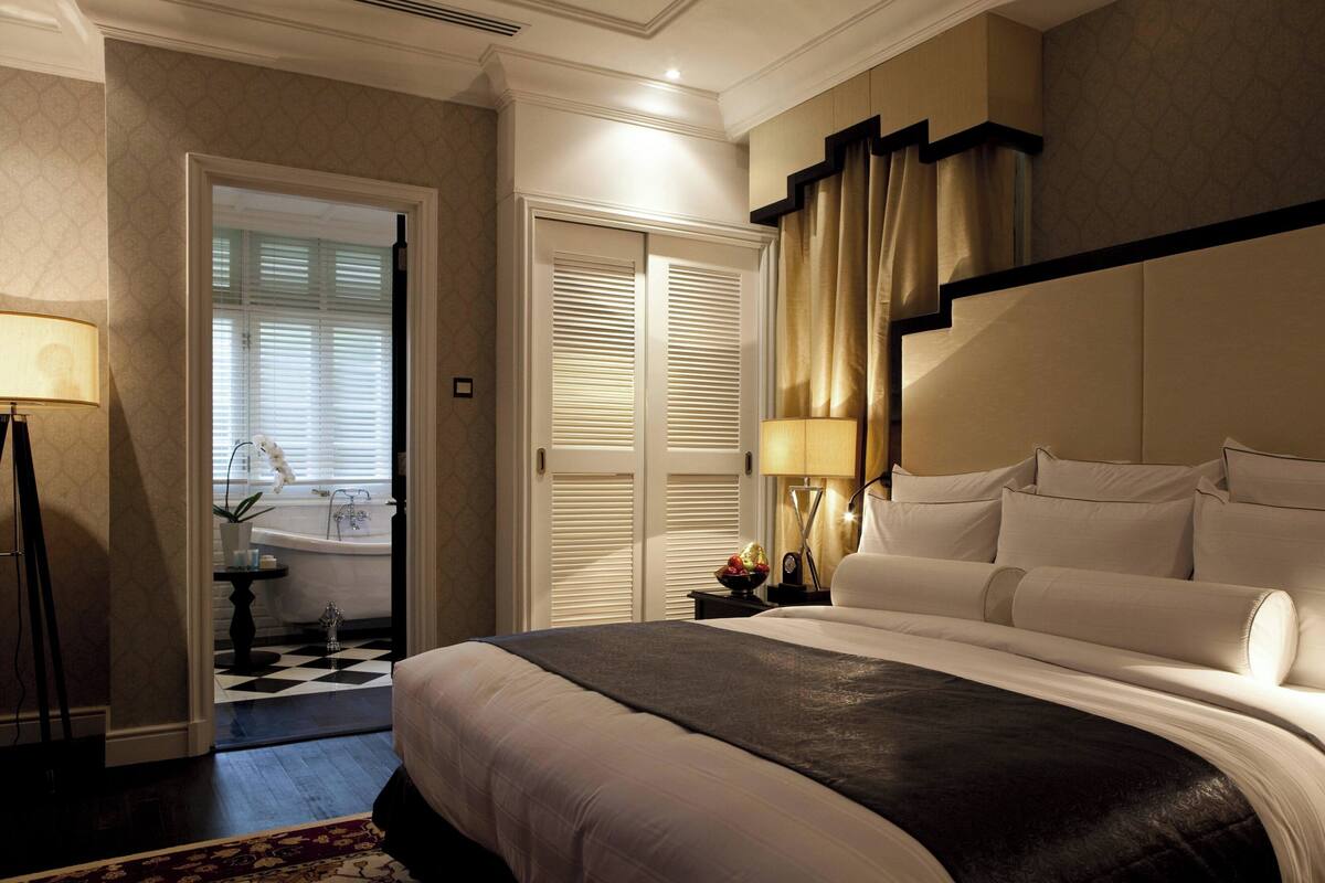 A hotel room with a large bed, a bedside table with a lamp, a bathroom with a bathtub, and a checkered floor.