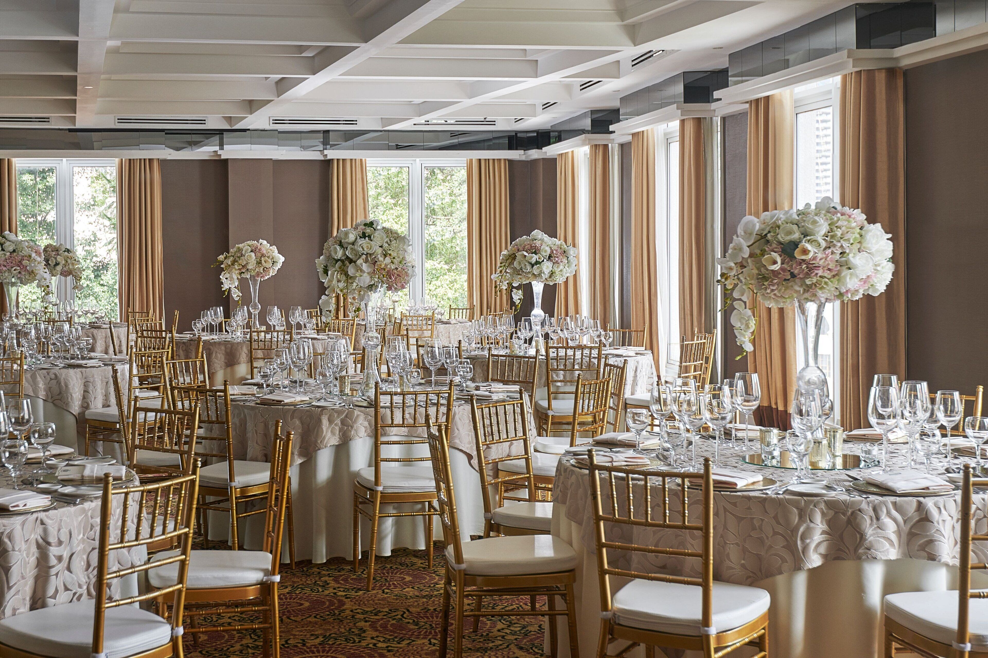A banquet hall with round tables, gold chairs, and floral centerpieces.