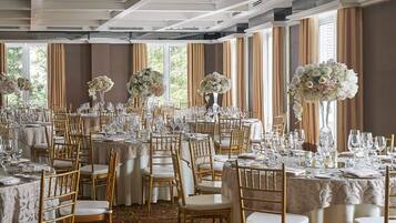 A banquet hall with round tables, gold chairs, and floral centerpieces.