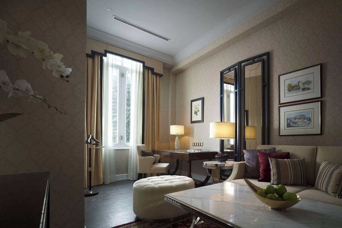 A hotel room with a sofa, a dining table, a lamp, and a mirror.