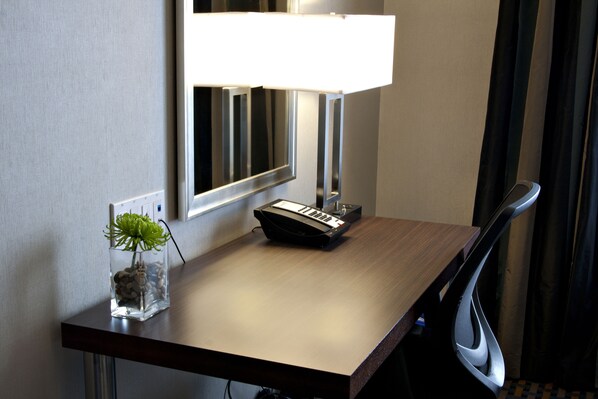 A hotel desk with a lamp, a small plant, and a telephone.