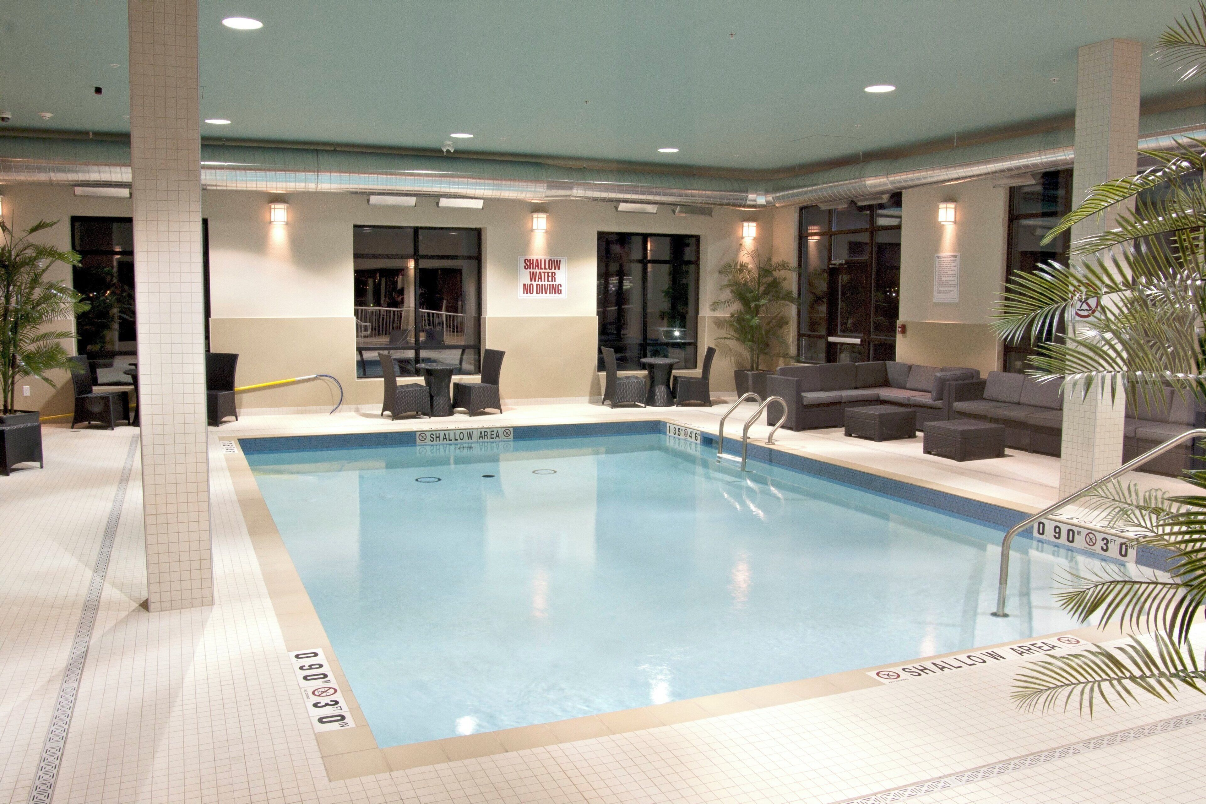 Une piscine intérieure dotée d’une zone peu profonde délimitée, entourée de sièges et accessible par un escalier.