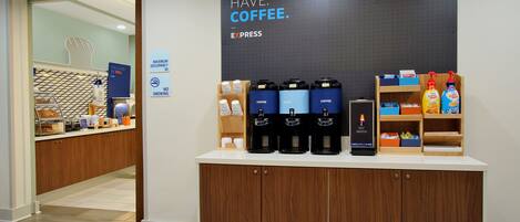 A coffee station with multiple coffee machines, a sign stating 'MUST HAVE COFFEE,' and a maximum occupancy sign.