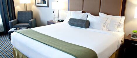 Habitación de hotel con una cama grande, una silla, una mesita de noche con lámpara y un cuadro en la pared.