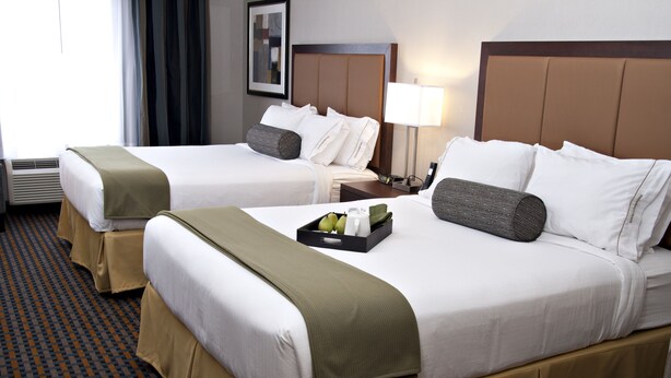 Two double beds with white linens, brown headboards, and beige bed skirts. There is a tray with a bottle and glasses on the bed. - Holiday Inn Express Pembroke by IHG (Pembroke)